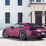 Low angle rear three quarter commercial photography of a Ruby Star Neo Porsche 911 GT3 parked in front of modern minimalist white architecture